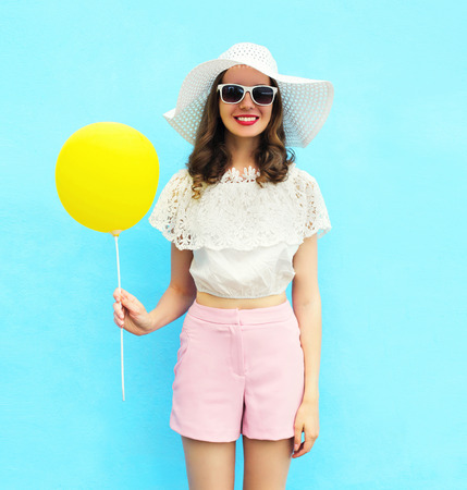 Fashion pretty woman in straw hat with air balloon over colorful blue backgroundの写真素材