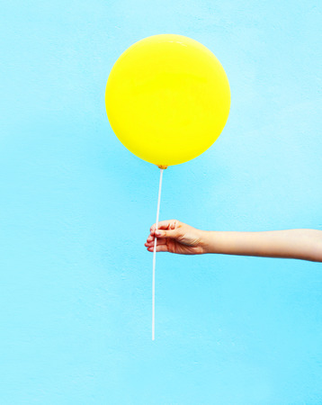 Hand holding yellow air balloon over colorful blue backgroundの写真素材