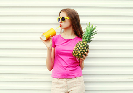 Fashion pretty cool girl with pineapple drinking from cup over white backgroundの写真素材