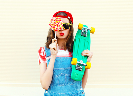 Portrait fashion pretty cool girl with lollipop and skateboard over white backgroundの写真素材