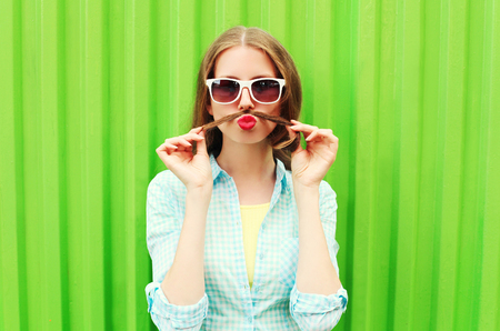 Woman having fun shows moustache hair over green backgroundの写真素材