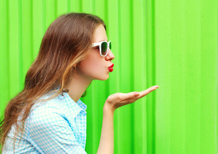 Woman in sunglasses sends an air kiss over colorful green backgroundの写真素材