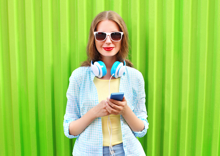 Beautiful woman listens to music in headphones using smartphone over green backgroundの写真素材