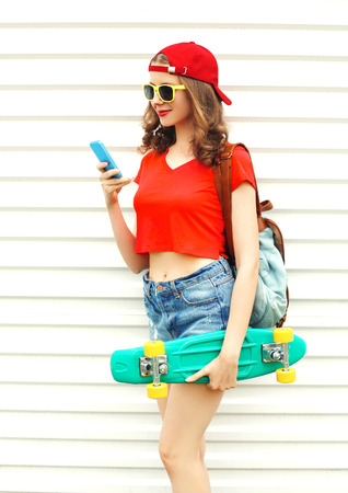 Fashion pretty cool smiling woman with skateboard using smartphone over white backgroundの写真素材