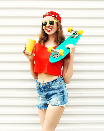 Fashion pretty cool woman with skateboard and cup of fruit juice over white backgroundの写真素材