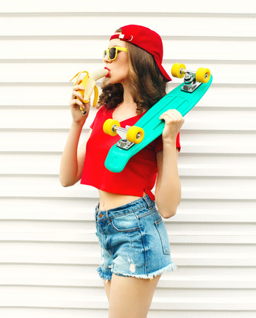 Fashion pretty cool woman with skateboard eating a banana over white backgroundの写真素材