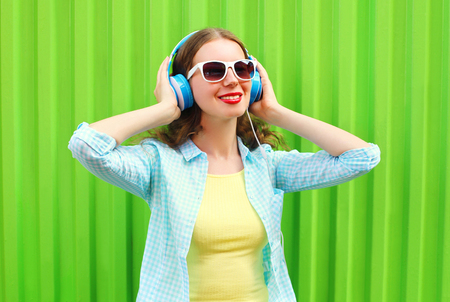 Happy pretty cool woman listens to music in headphones over green backgroundの写真素材