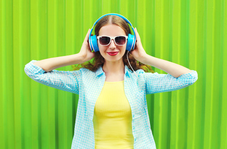 Happy pretty smiling woman listens to music in headphones over green backgroundの写真素材
