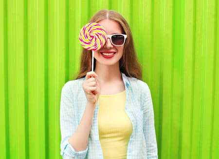 Portrait happy pretty smiling woman and lollipop over colorful green backgroundの写真素材