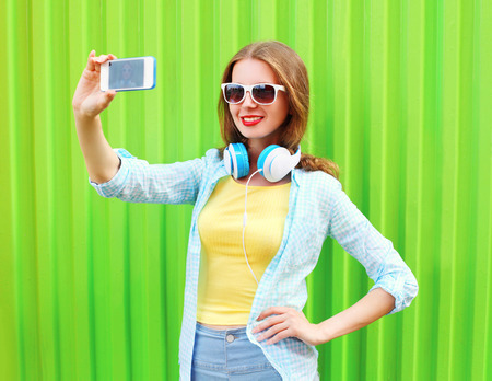 Pretty cool girl makes self portrait on smartphone over green backgroundの写真素材