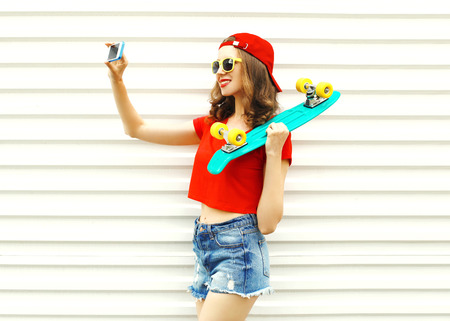 Pretty cool smiling girl makes self portrait on smartphone over white backgroundの写真素材