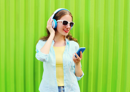 Pretty cool woman listens to music in headphones using smartphone over green backgroundの写真素材