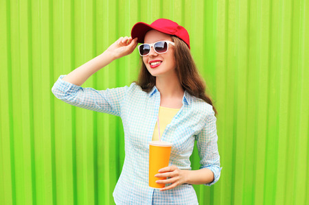 Pretty smiling woman in sunglasses with cup of fruit juice over colorful green backgroundの写真素材
