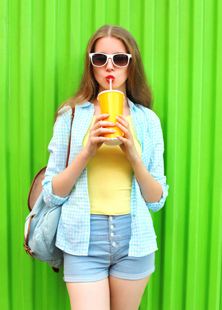 Pretty woman in sunglasses drinking fruit juice from cup over colorful green backgroundの写真素材