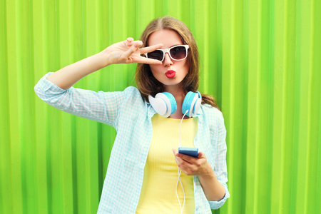 Pretty woman listens to music in headphones and using smartphone over green backgroundの写真素材
