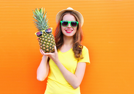 Pretty cool girl in sunglasses with pineapple having fun over colorful orange backgroundの写真素材