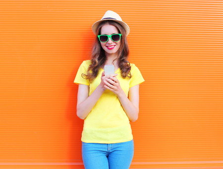 Pretty smiling woman using smartphone over colorful orange backgroundの写真素材