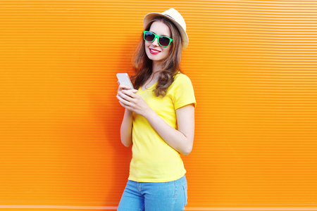 Pretty woman using smartphone over colorful orange backgroundの写真素材