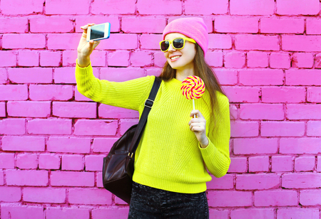 Fashion girl taking photo selfie portrait using smartphone over colorful pink backgroundの写真素材