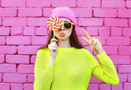 Fashion portrait pretty cool girl with lollipop having fun over colorful pink backgroundの写真素材