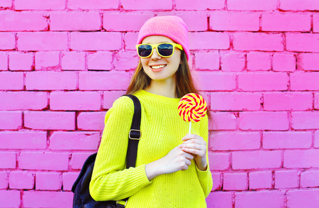 Fashion portrait pretty smiling girl with lollipop over colorful pink backgroundの写真素材