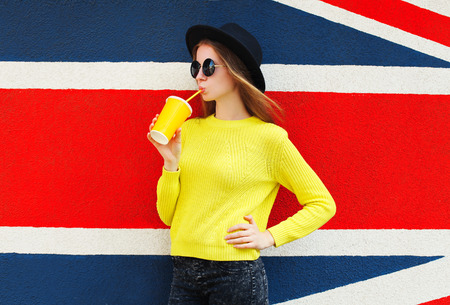 Fashion pretty woman with cup drinking over colorful urban backgroundの写真素材