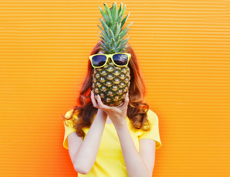 Fashion portrait woman and pineapple with sunglasses over colorful orange backgroundの写真素材