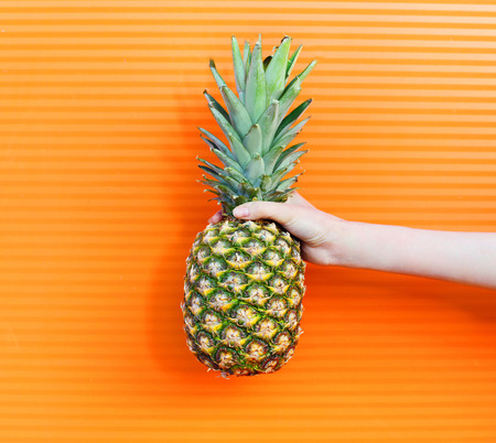 Hand and fruit pineapple over colorful orange background