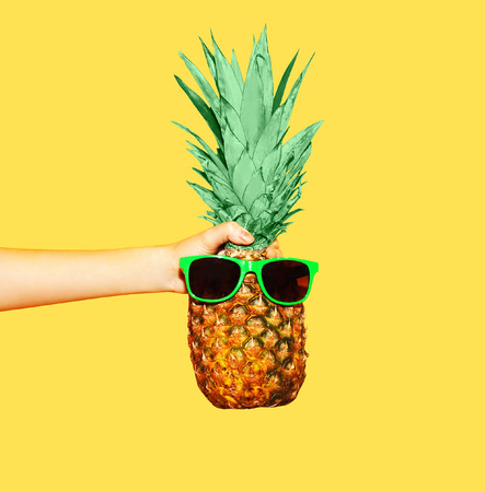 Fashion pineapple with sunglasses on yellow background, hand holding ananasの写真素材