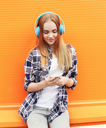 Pretty girl in headphones listens to music and using smartphone over orange backgroundの写真素材