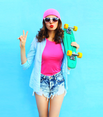 Fashion pretty cool woman in pink clothes with skateboard over colorful blue backgroundの写真素材