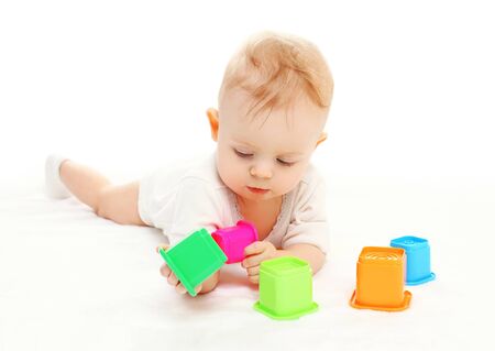 Baby lying playing with colorful toys on white backgroundの写真素材