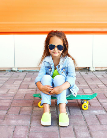 Beautiful little girl child sitting on skateboard in cityの写真素材