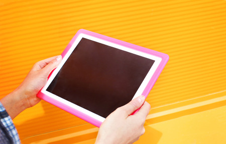 Female hands holding using digital tablet pc over colorful orange backgroundの写真素材