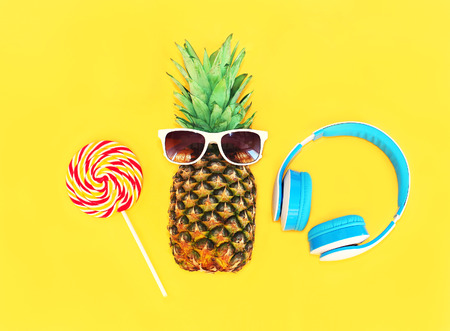 Fashion pineapple with sunglasses lollipop caramel and headphones over colorful yellow backgroundの写真素材