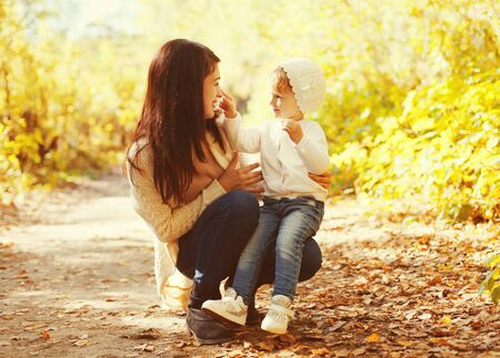 Happy smiling mother playing with child in warm autumn dayの写真素材