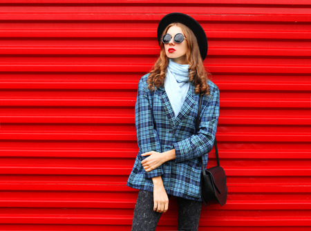 Fashion pretty woman wearing a black hat coat jacket and handbag over colorful red backgroundの写真素材