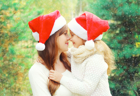 Christmas family child hugging mother in santa red hats together over a treeの写真素材