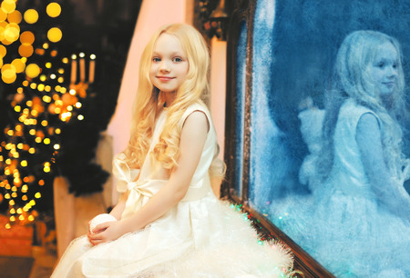 Happy child little girl with snowball toy over christmas tree bokeh at home near windowの写真素材