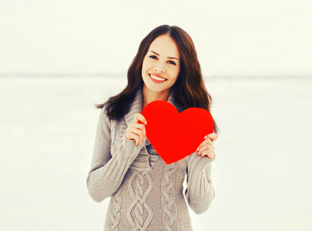 happy young smiling woman with big paper red heart in winter dayの写真素材