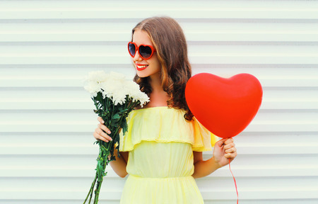 happy smiling woman holding bouquet flowers and red air balloon heart shape over white backgroundの写真素材