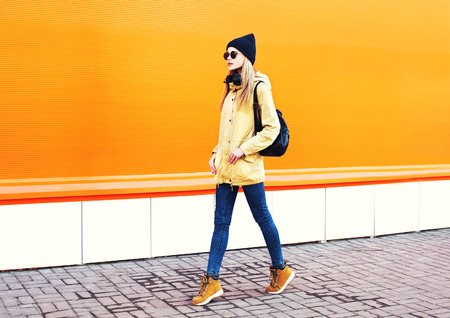 Fashion pretty blonde woman walking in city on a orange colorful backgroundの写真素材