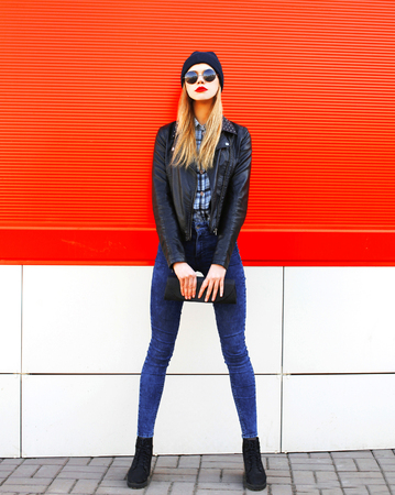 Fashion beautiful blonde woman in rock black style with clutch handbag on a red backgroundの写真素材