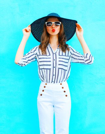 Fashion portrait young woman wearing a straw hat, white pants over colorful blue background posing in the cityの写真素材