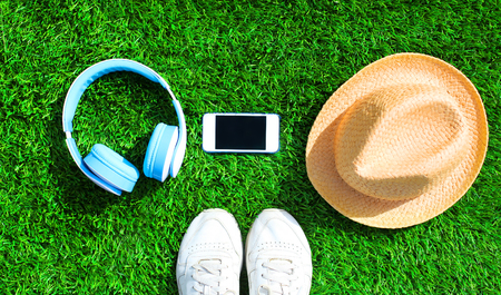 Blue headphones and white smartphone with straw hat on a green grass textured background, top view, flat lay photoの写真素材