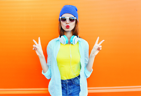 Fashion pretty young woman is blowing her red lips in the city over colorful orange backgroundの写真素材