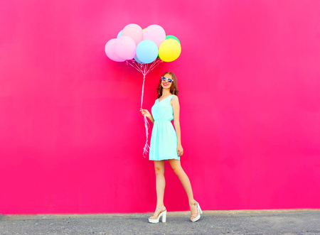 Happy smiling woman with an air colorful balloons walking over a pink backgroundの写真素材