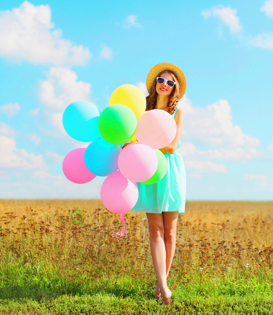 Happy pretty woman with an air colorful balloons enjoying a summer day on a meadow blue skyの写真素材