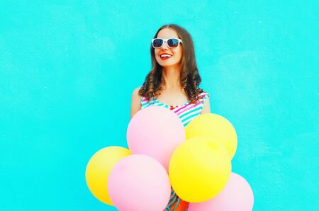 Happy smiling woman dreams with an air colorful balloons is having fun on a blue backgroundの写真素材