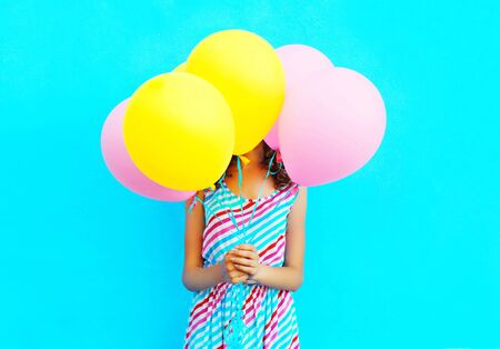 Woman is hides her head an air colorful balloons having fun over a blue background